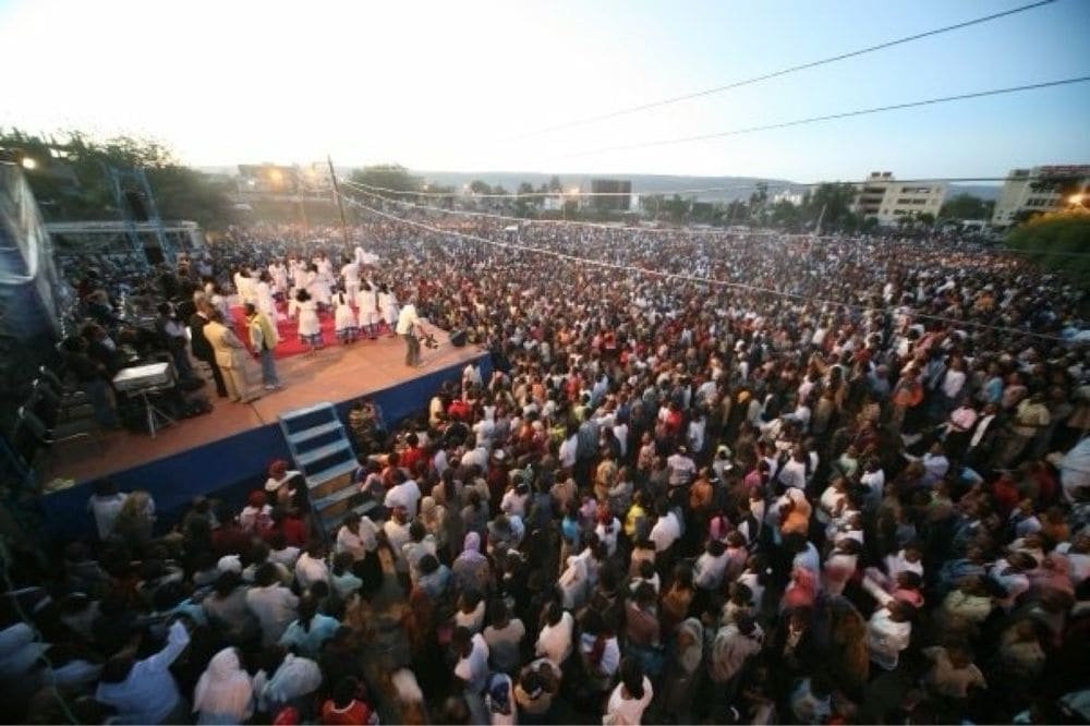 A large dusk crusade crowd before a stage with a choir in white robes