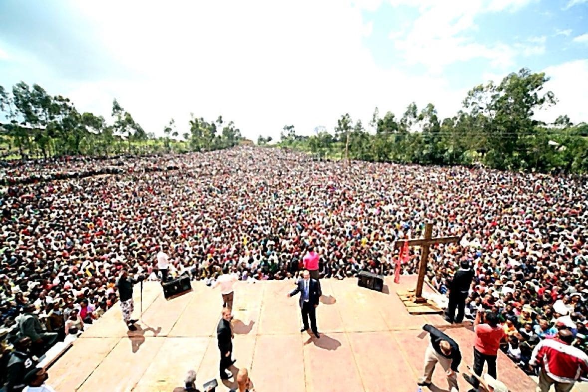 A massive historic crowd seen from the stage beside a wooden cross
