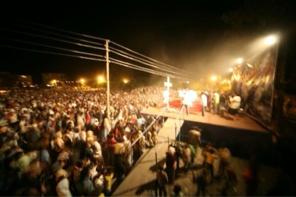 A night crusade with a lit stage, wooden cross and gathered crowd
