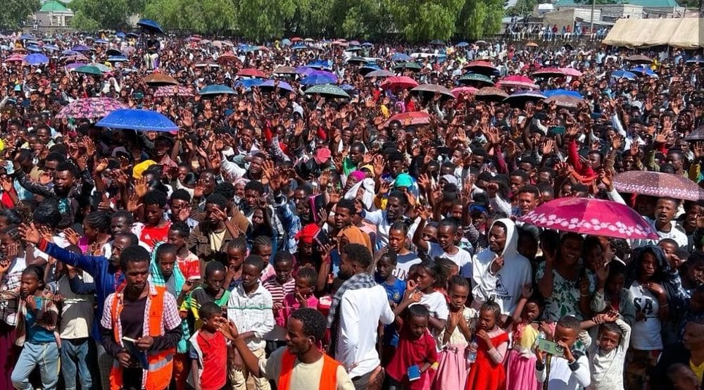 A dense historic crowd raising hands during a campaign