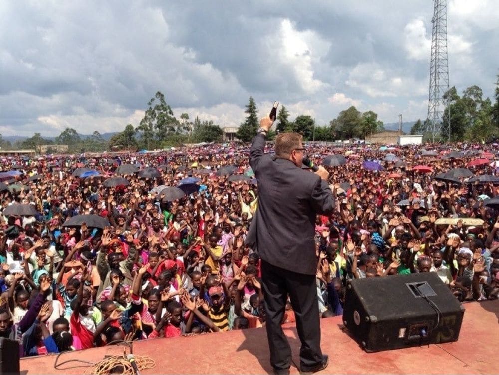 Karl Härgestam preaching with a Bible raised before a crowd holding umbrellas