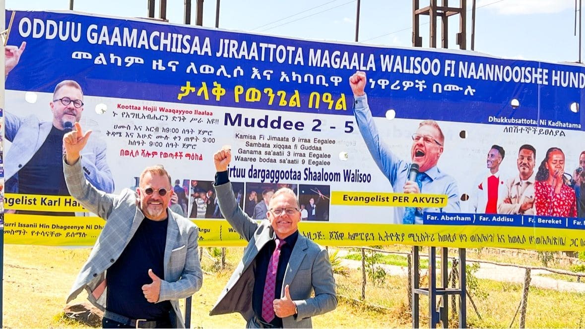 Karl Härgestam and Per Åkvist standing in front of an outdoor campaign billboard announcing Evangelist Per Åkvist